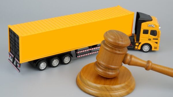 Wooden gavel and yellow cargo truck on grey background.