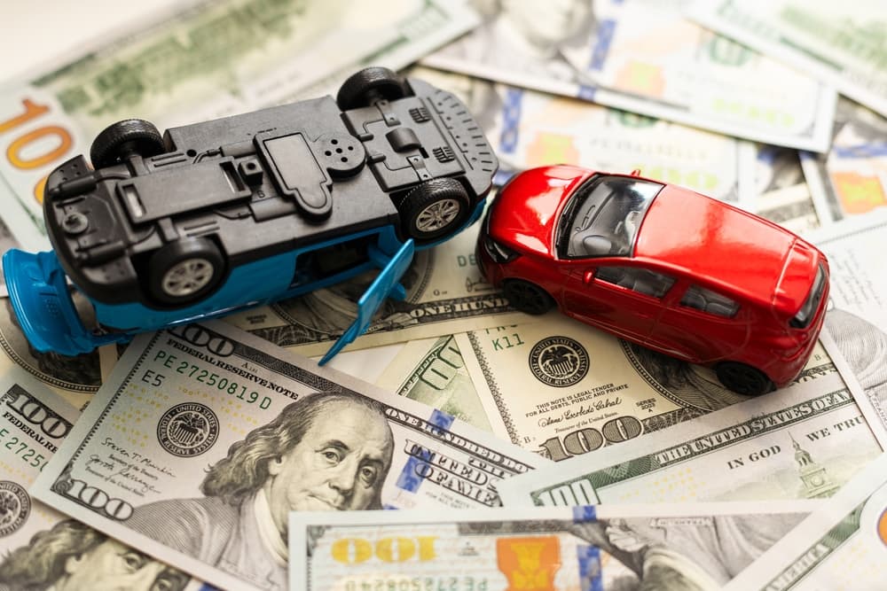 Two model cars on the heap of us hundred dollars.
