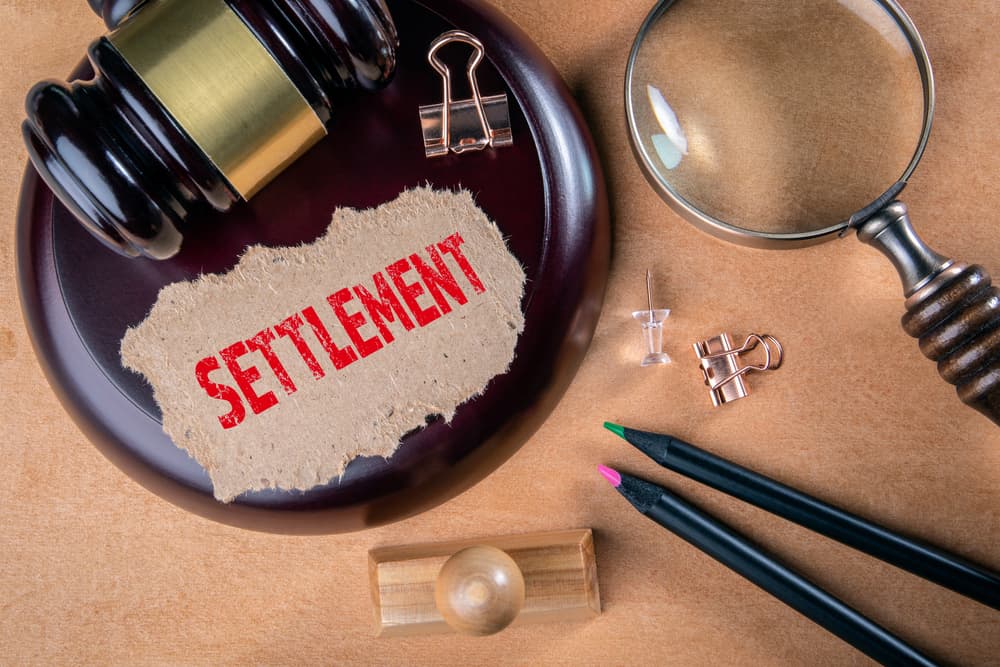 Wooden court hammer and magnifying glass on the table along with written settlement on a piece of paper