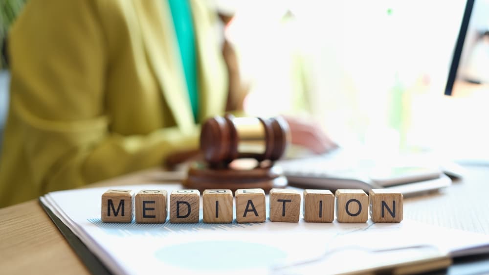 A mediator sitting near a judge's gavel, with the words "mediation" in close-up. Concept of judicial settlement of conflicts.