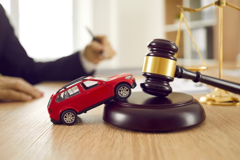 Small car model on wooden desk with judge's hammer.