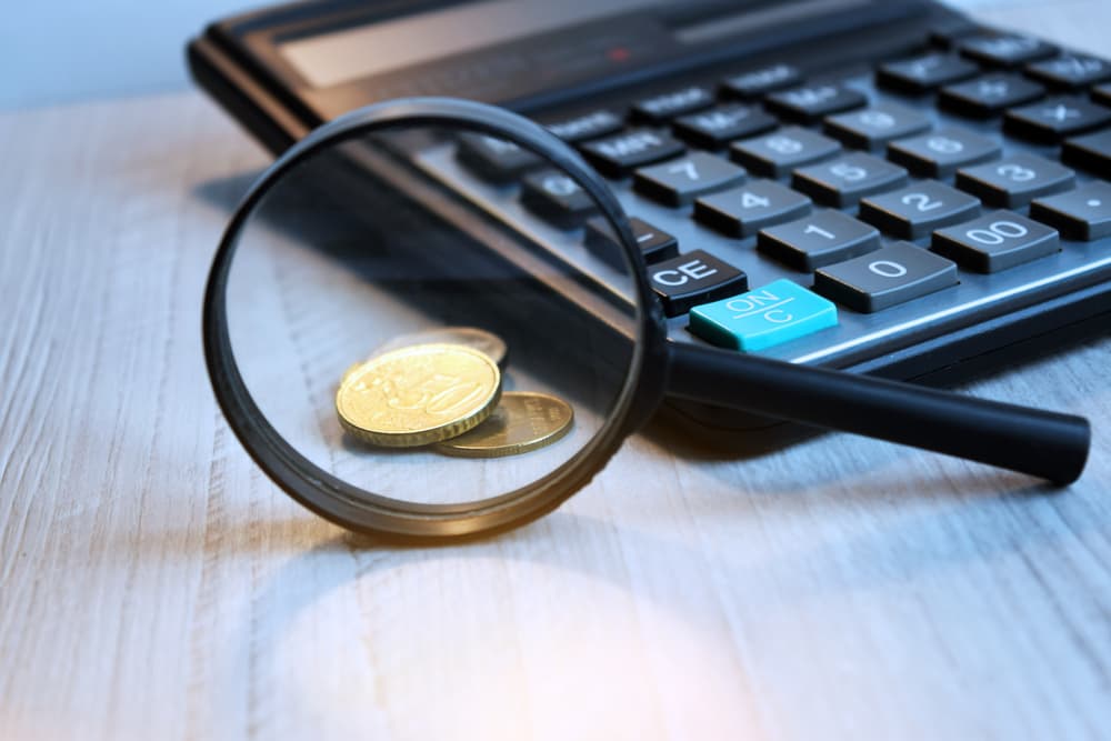 Conceptual image of business accessories on an office desk: a magnifying glass, manners book, and calculator, all in black and white with a soft focus.