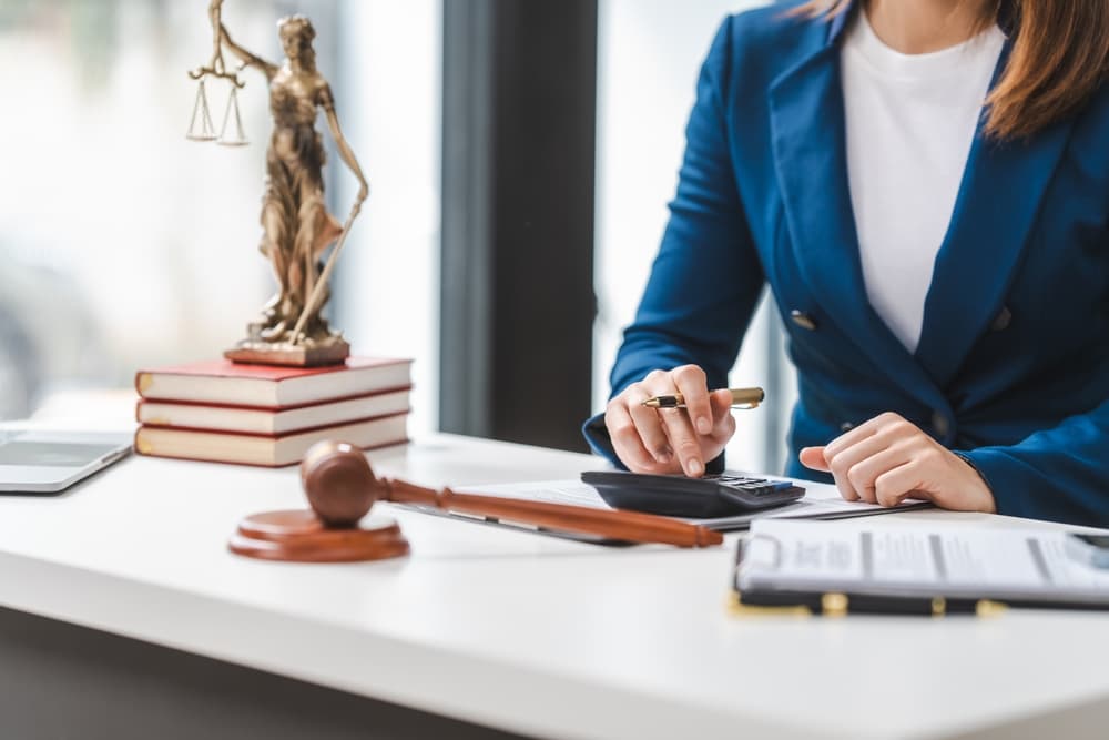 Lawyer calculating expenses, with a legal contract, gavel, and law books on the table.