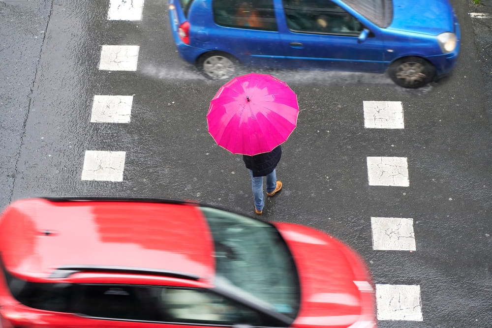 Pedestrian crossing a marked crosswalk between moving vehicles in the rain in San Jose, where a government entity claim must be filed within six months of the accident