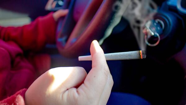 Driver holding a lit cigarette while behind the wheel, highlighting distracted and unsafe driving behavior.
