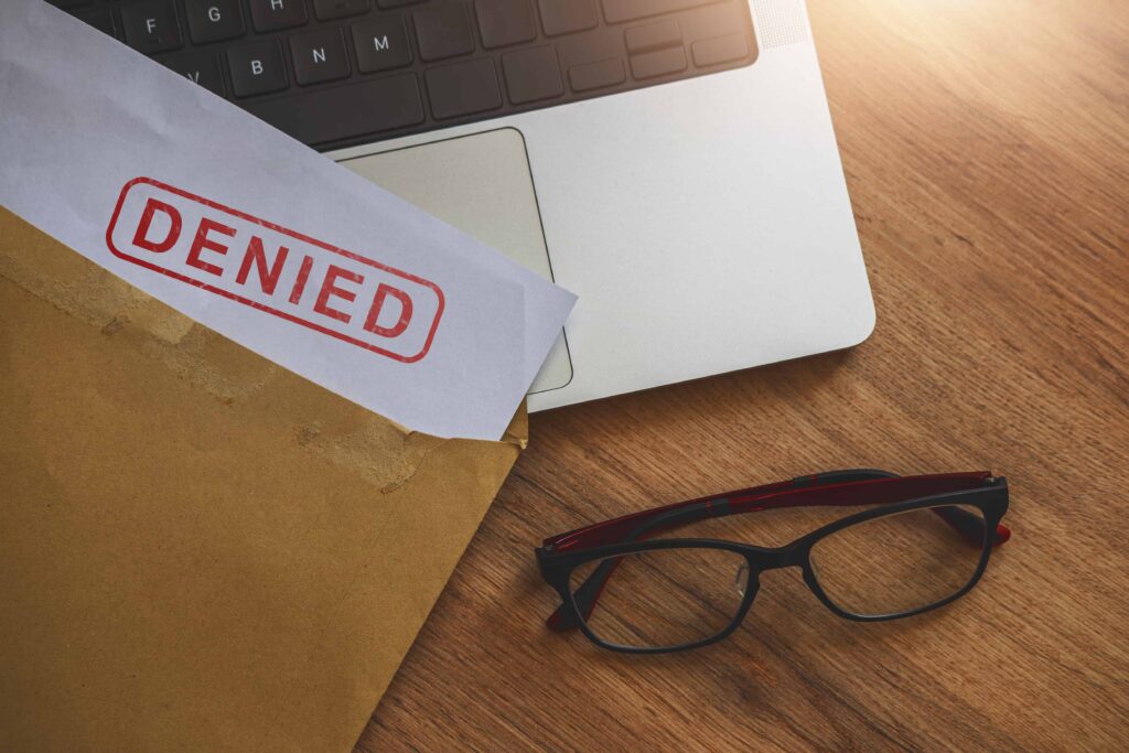 Denied claim letter in an envelope on a desk next to a laptop and eyeglasses.