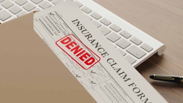 Denied insurance claim form in an envelope on a desk beside a computer keyboard and pen.