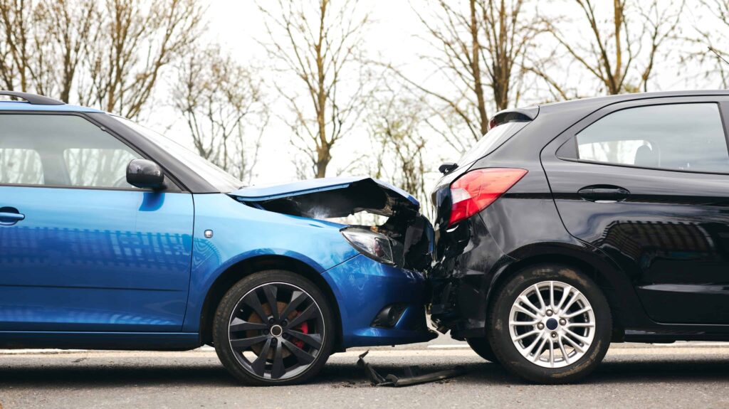 Blue car rear-ends black car in traffic accident showing vehicle damage from rear-end collision.