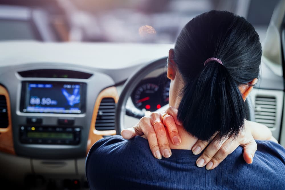 An Asian woman experiencing pain in her shoulder and neck while driving.






